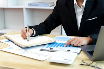 businesswoman Sitting at desk using smartphone and laptop with data from graph