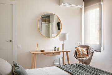 View from the bed is a cozy light-colored bedroom with wooden eco-furniture, console and mirror in...
