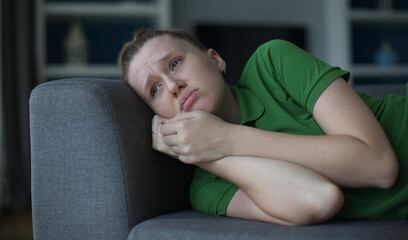 Worried young woman sit on sofa look aside lean forward with folded hands feel fear anxiety. Teen female stressed with unwanted pregnancy thinking on abortion hesitate have doubts making hard decision