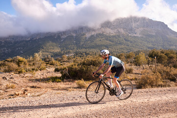 Cyclist practicing on gravel road.Fit male cyclist riding a gravel bike on a gravel road with a view of the mountains, Alicante region of Spain
