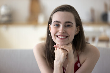 Happy pretty young adult girl in sleeveless cloth leaning chin on hands, looking at camera, posing...