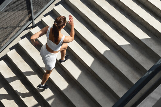 Athletic young woman runner in sportswear is training running up the stairs on sunny morning in the city top view. Healthy lifestyle concept
