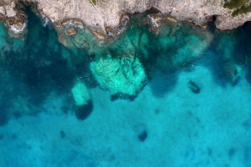 Summer holiday background. Top view of seascape with beautiful stone cliff and clear blue water on a sunny summer day. Sea coast, aerial drone shot. Travel concept