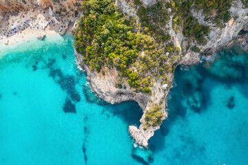 Naklejka premium Summer holiday background. Top view of seascape with beautiful coastline and small sandy beach with crowd of people on summer day. Sea coast with blue, turquoise clear water, aerial drone shot
