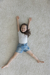 Happy adorable little girl relaxing on clean soft carpet. Cheerful sweet kid lying on back on...