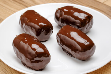 Chocolate dessert in a shiny glaze on a white plate standing on a wooden table. 