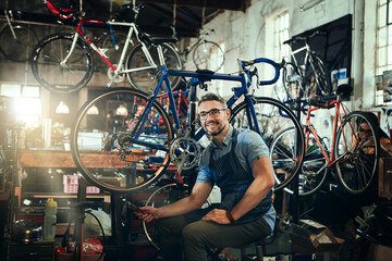 Portrait, wrench and smile of repair man in bicycle shop, store or cycling workshop. Face, bike mechanic and male person, happy business owner or mature technician with glasses and confidence.