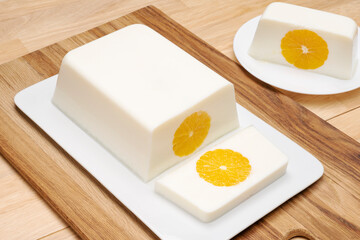 Milk orange jelly square shape on a white platter on a wooden table. 