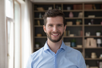 Happy handsome young Caucasian business man head shot portrait. Positive attractive male model with stubble wearing pale blue office shirt, looking at camera with toothy smile