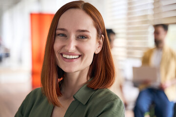 Closeup portrait of attractive smiling red haired student standing in university campus, education concept. Confident businesswoman, successful manager looking at camera