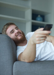 Fototapeta premium portrait of joyful young man in casual clothes sitting and lay on sofa in living room and looking tv with remote control in hand at home 