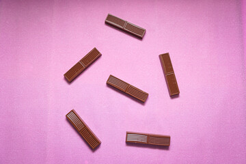 Broken milk chocolate on pink background.