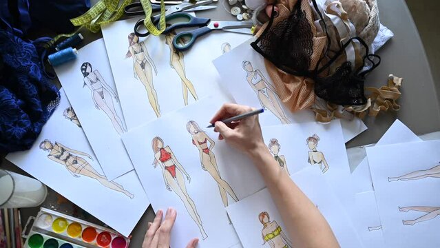 Faceless woman draws sketches of swimwear with a pencil. Top view of the hands of a fashion designer.