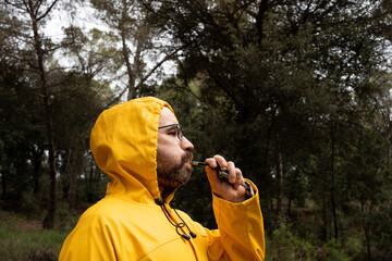 portrait of a man in a bright yellow raincoat with hood in the middle of the forest calling the dog...
