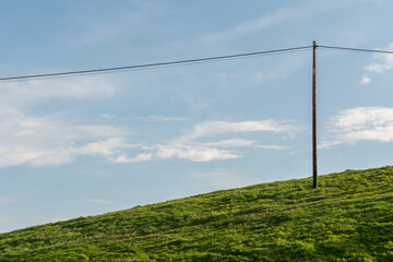 Fototapeta na wymiar A lone electricity pole on a green hill