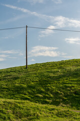 Fototapeta na wymiar A lone electricity pole on a green hill