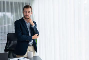 Handsome businessman in black suit stand confidently in his modern office portrait, deep in thought...