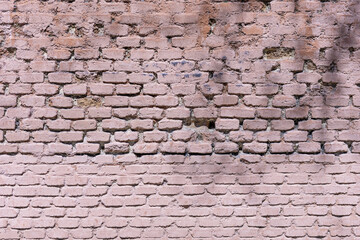 An old brick wall with deformities painted in a pale pink color