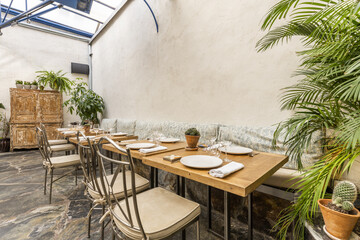 Wooden dining tables of a restaurant with indoor plants and metal chairs