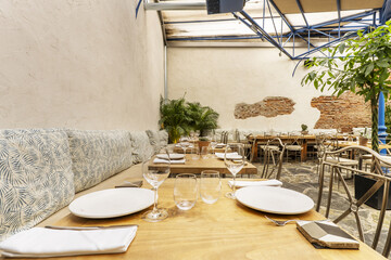 Wooden dining tables of a restaurant with houseplants and metal chairs with cushions