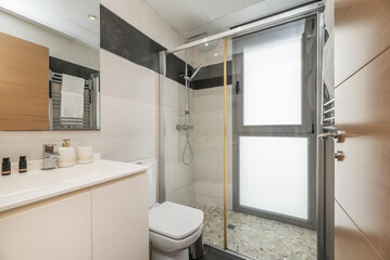 A small bathroom with a shower cabin with a stone floor, a white cabinet with a sink