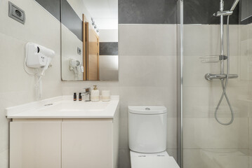 A small bathroom with a walk-in shower with a stone floor, a white cabinet with a sink, a wall-mounted hairdryer