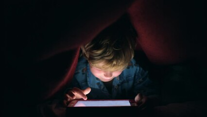 Night, light and tablet with child with blanket after bedtime for internet, movie and technology for streaming service. Relax, learning and digital with boy in bedroom hiding and playing online games - Powered by Adobe