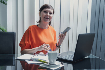 Mujer de negocios sonriente y feliz trabajando con su teléfono móvil y ordenador portatil en la...