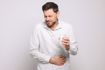Man with glass of milk suffering from lactose intolerance on white background