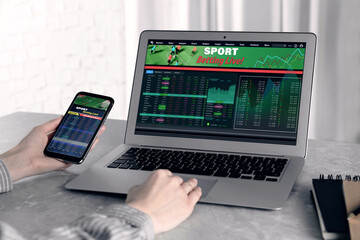 Woman betting on sports using smartphone and laptop at table, closeup. Bookmaker websites on displays