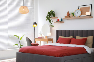 Stylish bedroom interior with comfortable bed, dressing table, lamps and green houseplants