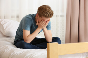 Unhappy teenage boy covering face with hands on bed at home
