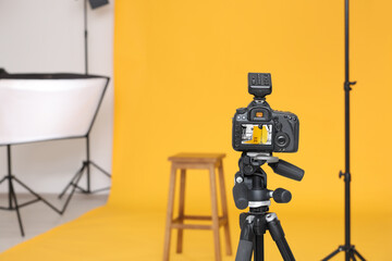 Camera on tripod, bar stool and professional lighting equipment in modern photo studio, space for text