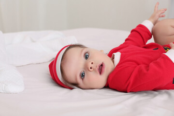 Cute baby wearing festive Christmas costume on bed