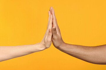 International relationships. People giving high five on orange background, closeup