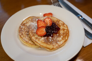 Homemade American pancakes served with strawberry jam and fresh ripe strawberries on a white board, sweet dessert