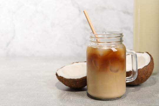 Mason jar of delicious iced coffee with coconut syrup on light grey table. Space for text