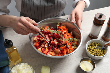 Woman preparing tasty vinaigrette salad at light wooden table, closeup