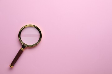 Magnifying glass on pink background, top view. Space for text