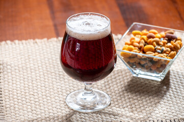 Glass of Belgian abbey red brown beer and glass bowl with party nuts