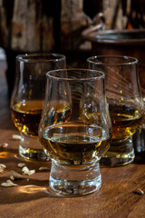 Small tasting glasses with aged Scotch whisky on old dark wooden vintage table with barley grains