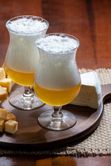 Glasses of Belgian light blonde beer made in abbey and wooden board with variety of belgian cheeses