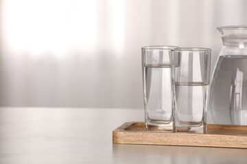 Glasses and jug with water on white table against blurred background. Space for text