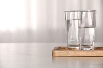 Glasses with water on white table against blurred background. Space for text - obrazy, fototapety, plakaty