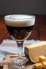 Glass of Belgian abbey brown beer and wooden board with old belgian cheese made by monks from cow milk