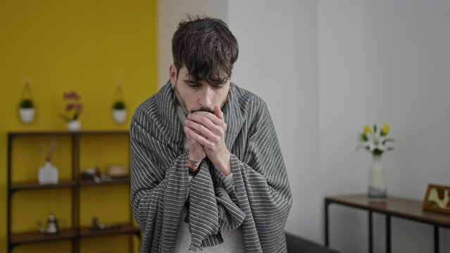 Young hispanic man feeling cold covered with blanket at home