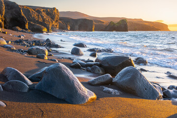Scenic beach with black sand by low tide at sunset. Sharp volcanic cliffs on Atlantic ocean coastline. Famous touristic place in Iceland