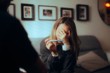 Sad Woman Holding a Pregnancy Test Informing her Partner. Stressed husband and wife trying to...