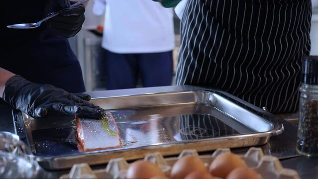 Closeup hands of chef preparing marinated slice salmon fish raw for cooking food while put ingredient and condiment at kitchen, meat and recipe for delicious, gastronomy seafood and nutrition.