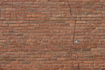 Full frame texture background of an old reddish brown clay brick wall with a common bond brickwork pattern, showing major cracking in its structure